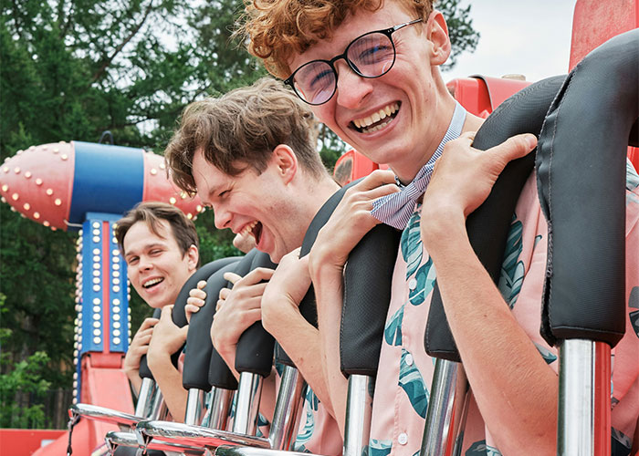 Three young men laughing on an amusement park ride, illustrating dumbest reasons that almost cost people their lives.
