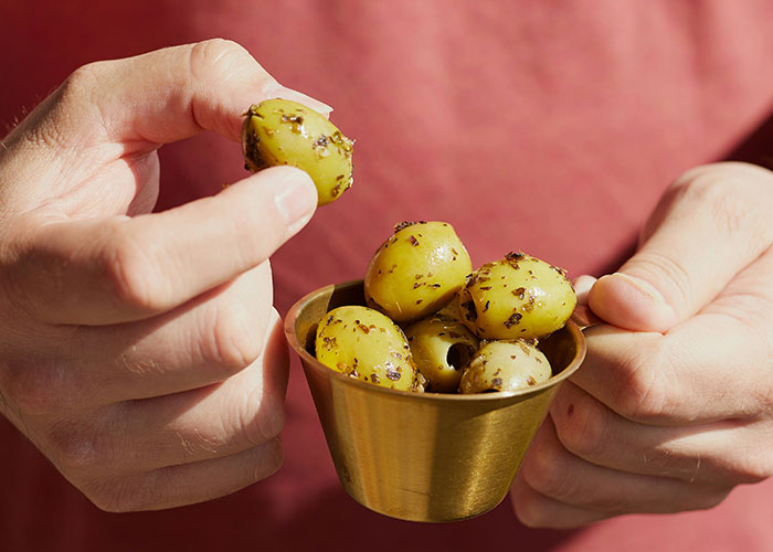 Close-up of hands holding a cup of olives covered in ants, illustrating dumbest reasons that almost cost people their lives.