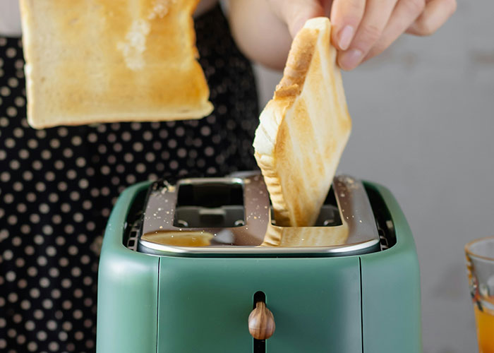 Person inserting burnt toast into a green toaster, illustrating one of the dumbest reasons that almost cost people their lives.