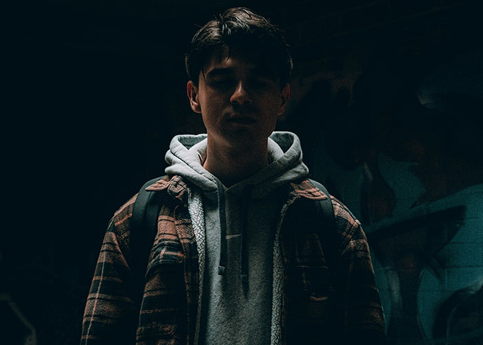 Young man in dark lighting wearing a hoodie and backpack representing dumbest reasons that almost cost lives.