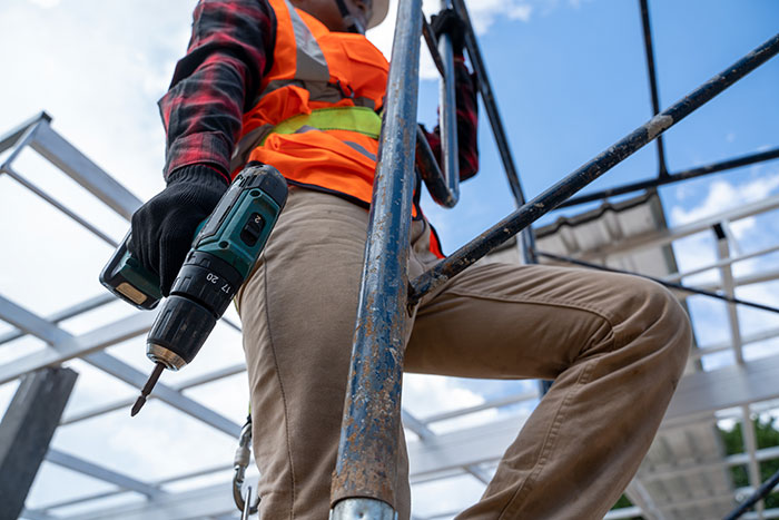Worker in orange safety vest holding power drill on scaffolding, symbolizing unexpected dramatic deathbed confessions and survival. - 9