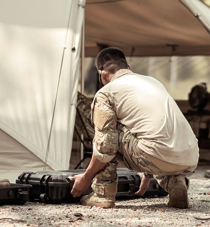 Soldier in camouflage gear crouching outdoors near a tent, illustrating dramatic deathbed confessions and survival stories. - 22