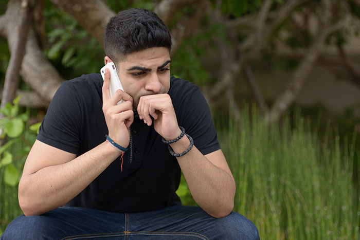 Young man in black shirt looking worried while making a dramatic deathbed confession on a phone call outdoors. - 4