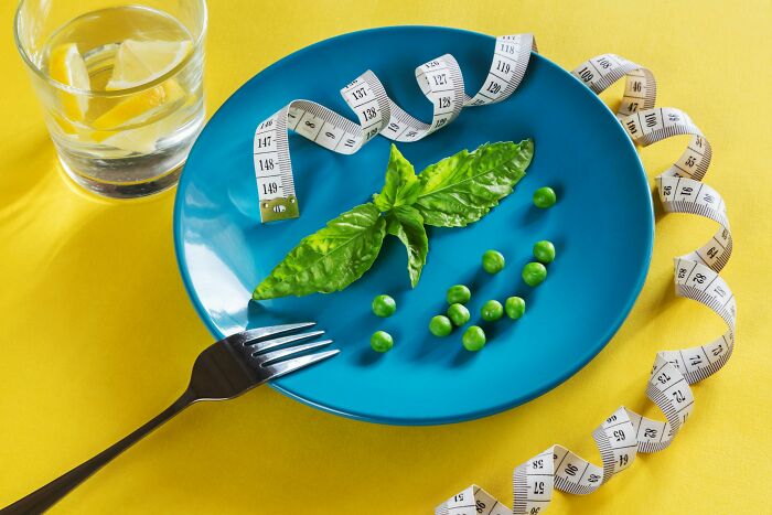 Blue plate with basil and peas, measuring tape wrapped around, fork nearby, and a glass of water, illustrating bizarre beliefs. - 28