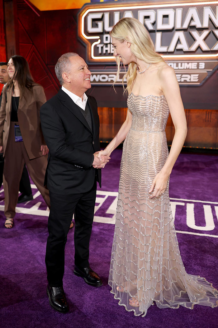Tall female star in a shimmering gown shaking hands with a man, showcasing unexpected super tall celebrity height difference.