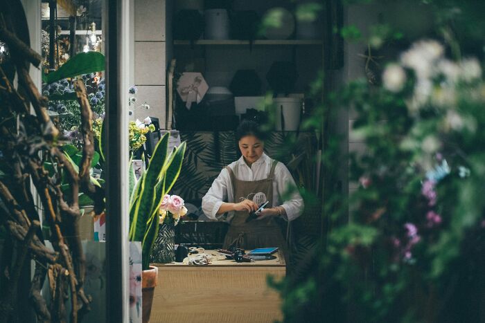 Woman working in a cozy florist shop surrounded by plants and flowers, illustrating romanticized red flag behaviors. - 17