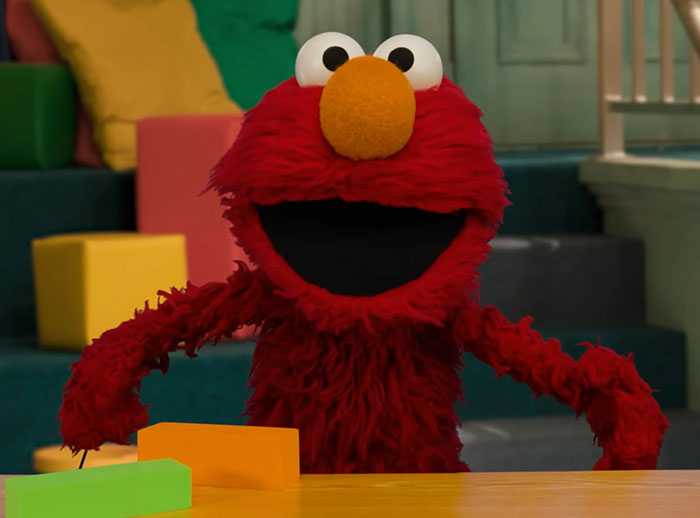 Elmo puppet sitting indoors with colorful blocks on table, related to violent messages on Elmo’s X account news. Elmo puppet sitting indoors with colorful blocks on table, related to violent messages on Elmo’s X account news.