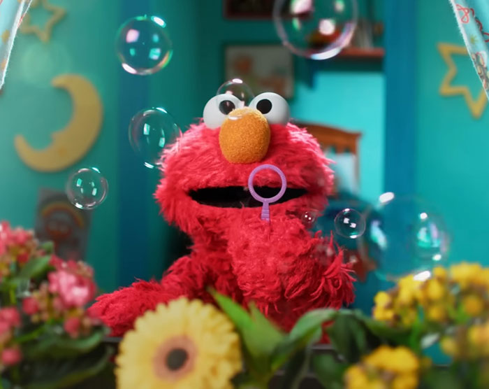 Elmo surrounded by bubbles and flowers in a colorful room, highlighting violent messages shared on Elmo's X account. Elmo surrounded by bubbles and flowers in a colorful room, highlighting violent messages shared on Elmo's X account.