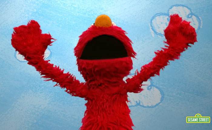 Elmo puppet with arms raised against a blue sky background, related to violent messages on Elmo’s X account warning. Elmo puppet with arms raised against a blue sky background, related to violent messages on Elmo’s X account warning.