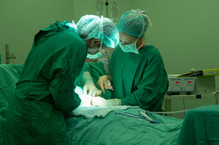 Two medical professionals in surgical scrubs performing a procedure in an operating room after birth.