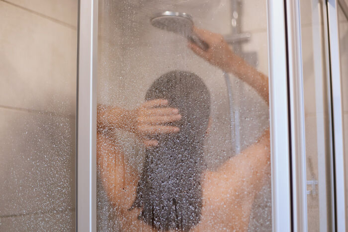 Person with long hair taking a shower behind a foggy glass door showing things non-Americans do that confuse Americans. - 45