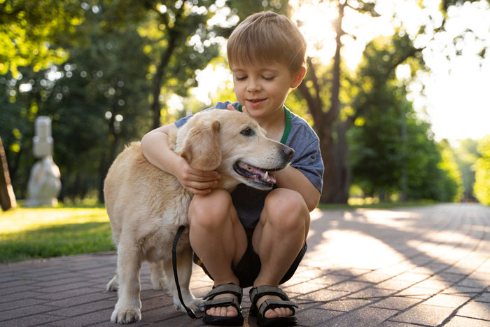 Young boy hugging a 6-year-old service dog outdoors, highlighting a family dispute over the late brother&rsquo;s dog.