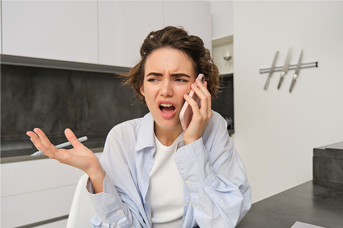 Young woman looking frustrated while talking on phone, expressing entitlement about rent payment from daughter-in-law.