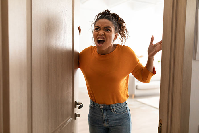 Angry woman confronting grifter neighbor, refusing to lend money, accused of starving her baby in tense doorway argument.