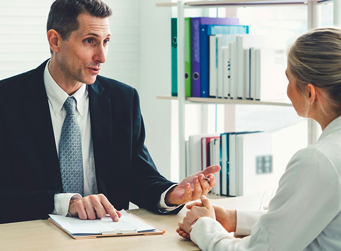 Man in suit discussing neighbors treating driveway like backyard with woman in office setting.