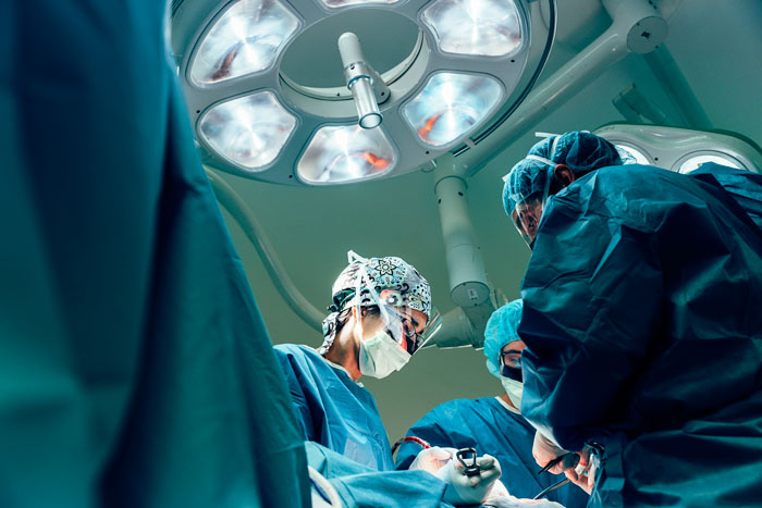Surgeons in scrubs and masks performing an operation under bright surgical lights in an operating room Surgeons in scrubs and masks performing an operation under bright surgical lights in an operating room
