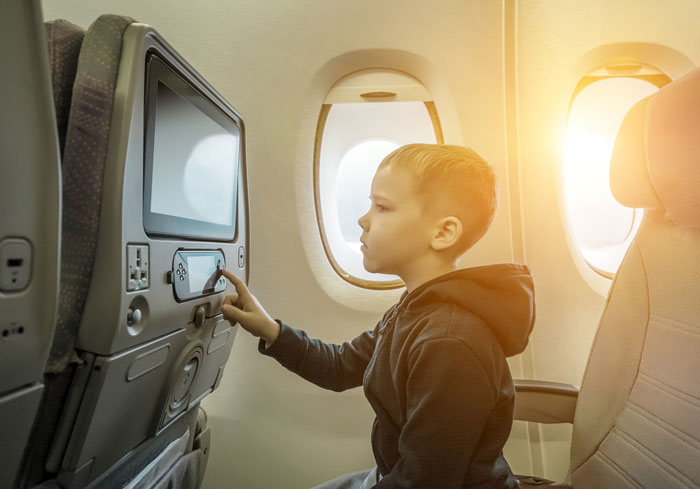Young boy in airplane seat using touchscreen entertainment system by the window during flight. Young boy in airplane seat using touchscreen entertainment system by the window during flight.