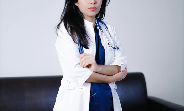 Woman denied plasma donation stands with arms crossed wearing white coat and stethoscope, conveying tension and frustration. Woman denied plasma donation stands with arms crossed wearing white coat and stethoscope, conveying tension and frustration.