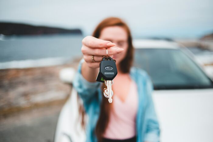 Woman holding car keys in front of a white vehicle near the coast, illustrating pettiest things in breakups.