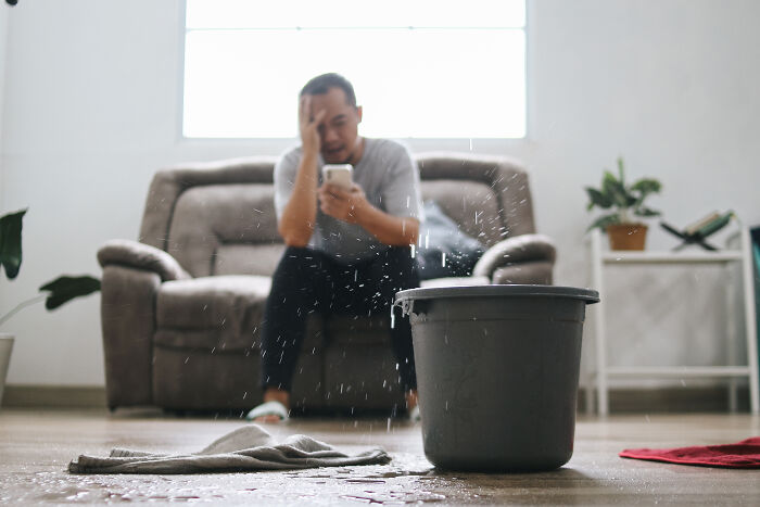 Man sitting on sofa looking stressed while water leaks into bucket, representing escape room employees stories. - 21