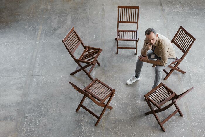 Man seated thoughtfully among empty wooden chairs in an open space, representing escape room employees stories. - 10
