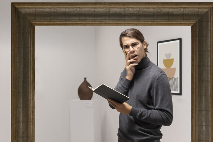 Young escape room employee wearing glasses, holding a notebook and looking puzzled while solving a story challenge indoors - 14