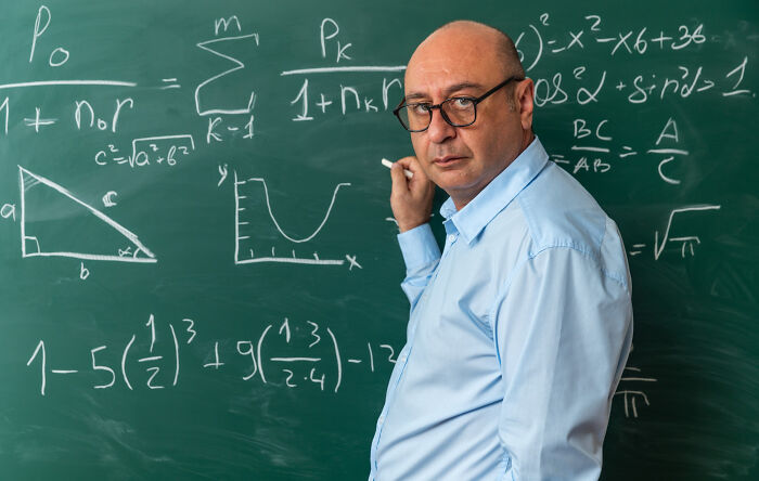 Escape room employee explaining complex math formulas on a chalkboard in an educational setting. - 16