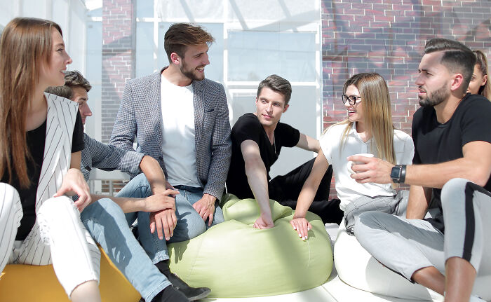 Group of escape room employees sharing stories and experiences in a bright, casual meeting setting with relaxed seating. - 23