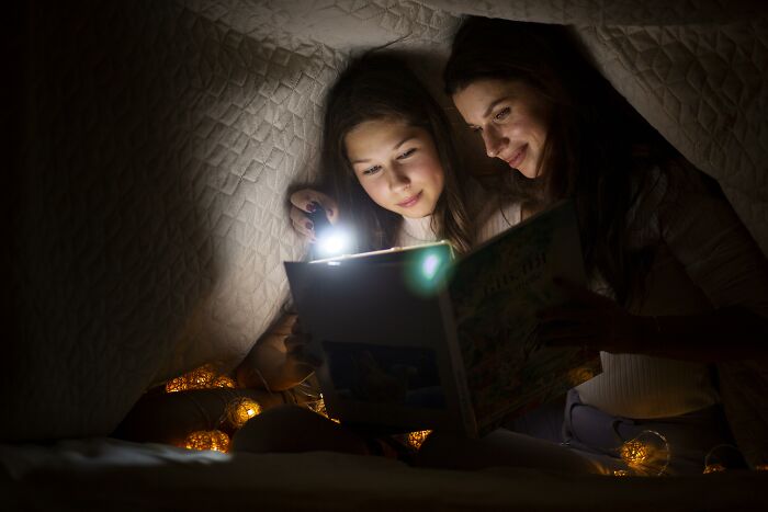 Two women using a flashlight under a blanket, immersed in an escape room employees stories activity at night. - 20