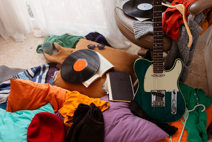 Guitar, vinyl records, clothes, and books scattered on the floor in a cozy escape room employees space. - 13