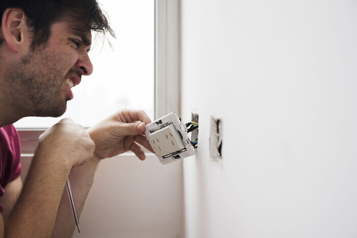 Man working on electrical wiring in a white room, illustrating escape room employees stories with hands-on technical tasks. - 9