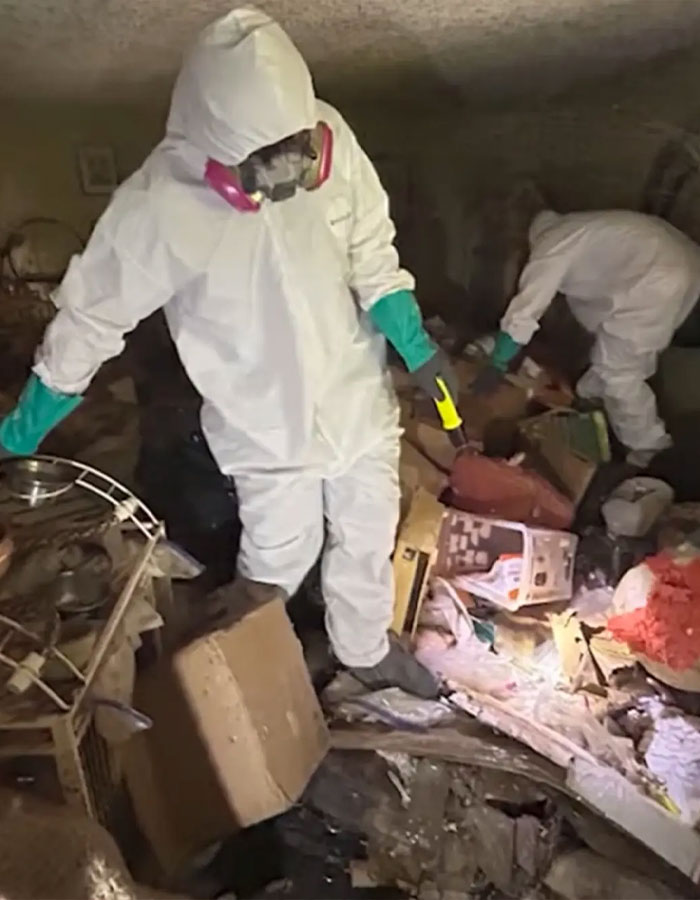 Forensic investigators in protective suits uncover skeletal remains amid trash in a hoarder ex-cop house investigation.