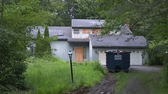 Overgrown yard and boarded-up hoarder house where police discovered skeletal remains beneath trash inside.