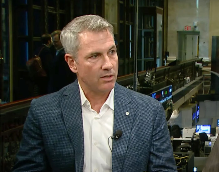 Middle-aged man in a checkered blazer discussing ex-employee's reaction to toxic CEO Coldplay kiss cam drama in office setting.