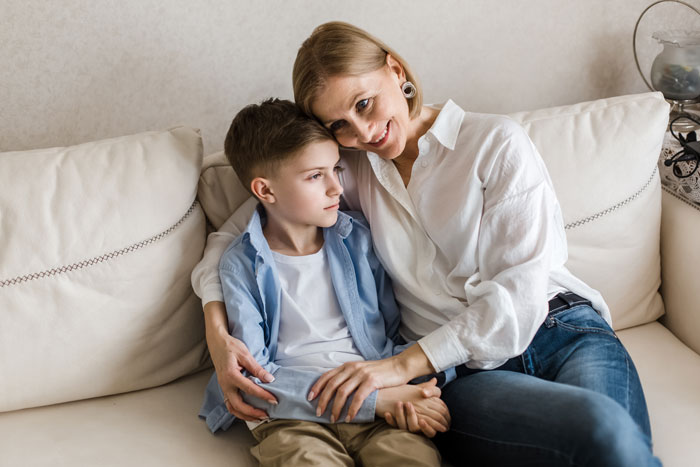 Woman sitting on a couch, holding and comforting a young boy, illustrating a stepkid relationship and bathroom refusal dispute.
