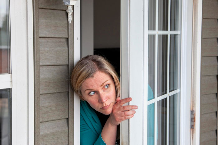 Woman peeking cautiously through a door, suspecting ex's stepkid wants to snoop, refusing bathroom access.