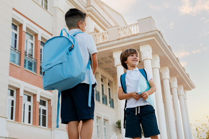 Two boys with backpacks standing outside a school building, illustrating a stepkid and bathroom refusal situation.
