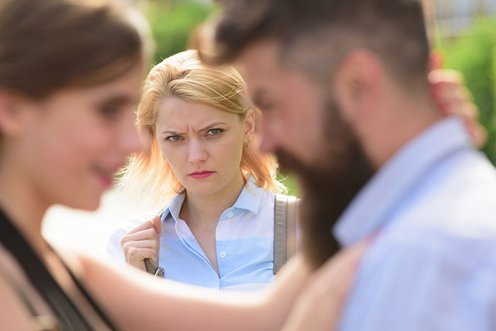 Woman looking upset while a man and another woman argue in the foreground, depicting family conflict and no-contact issues.