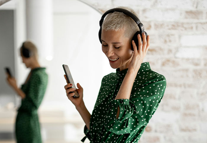 Woman in green polka dot dress enjoying music on headphones while holding phone, representing personal thoughtful gifts concept.
