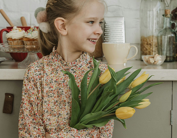 Young girl holding a bouquet of yellow tulips as a personal and thoughtful gift in a cozy kitchen setting.