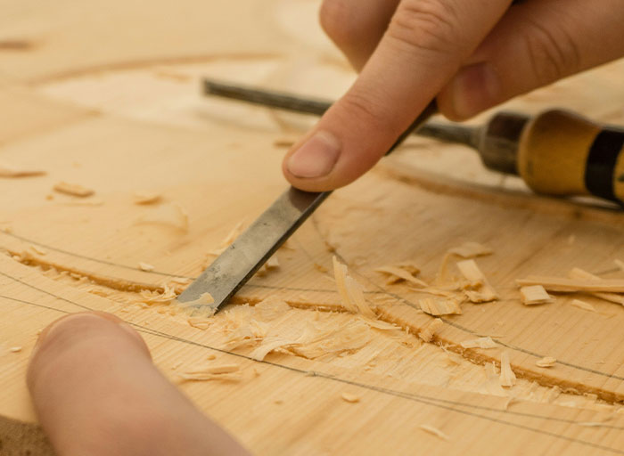 Close-up of hands carving wood with a chisel, showcasing personal and thoughtful gifts crafted by hand.