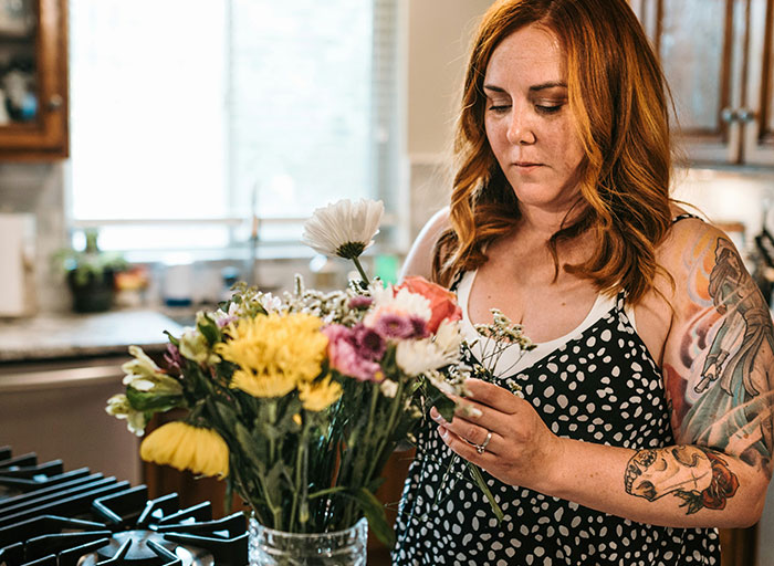 Woman with tattoos arranging a personal and thoughtful bouquet of colorful flowers in a kitchen setting.