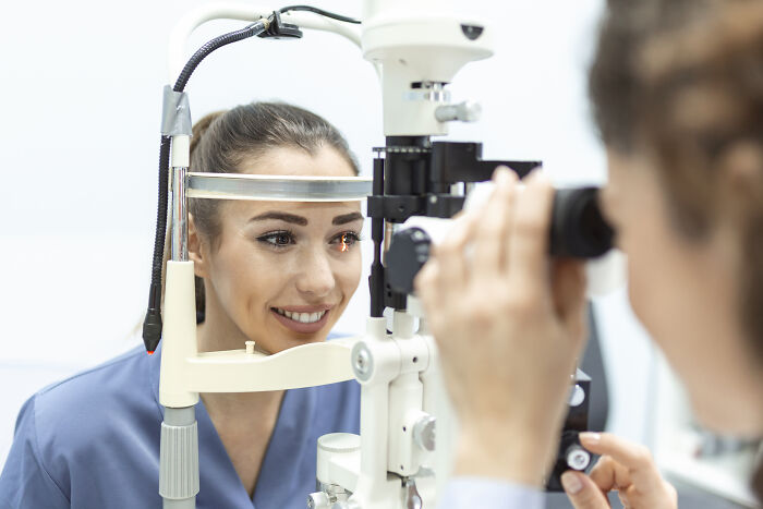 Female doctor examining a patient's eye using medical equipment, highlighting encounters with impostor patients needing common sense.