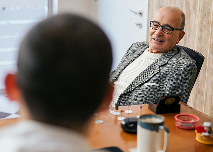 An elderly man wearing glasses and a checkered jacket talking to a doctor in an office about health concerns. - 30