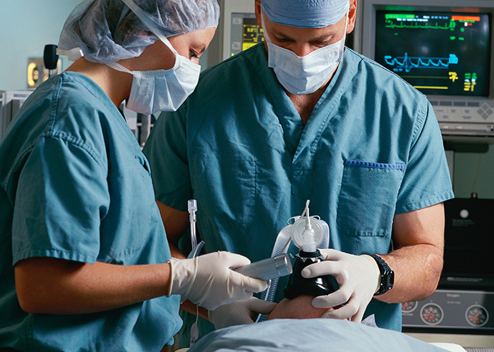 Two doctors in surgical scrubs and masks using medical equipment in an operating room with monitors in the background - 5