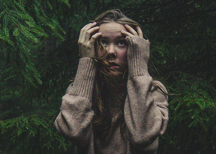 Young woman in a brown sweater looking anxious surrounded by dark green foliage, reflecting death machines concept. - 19