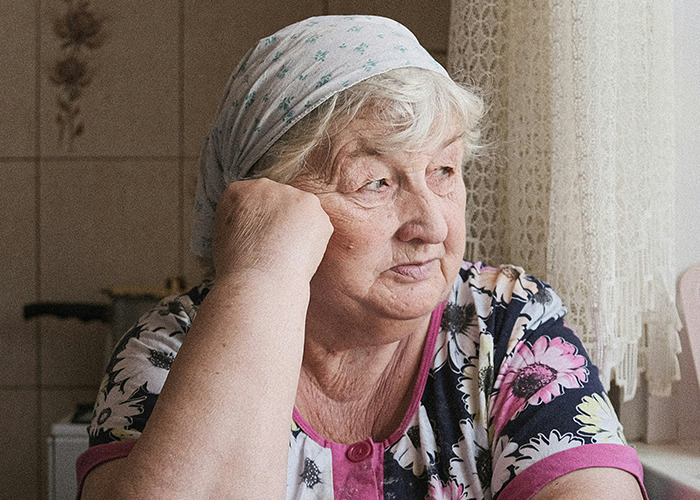 Elderly woman wearing a headscarf, looking thoughtfully out the window, symbolizing concerns about death machines. - 22