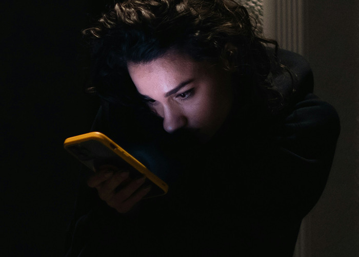 Person with curly hair looking intently at a phone screen in a dark room, illustrating concerns about death machines. - 31