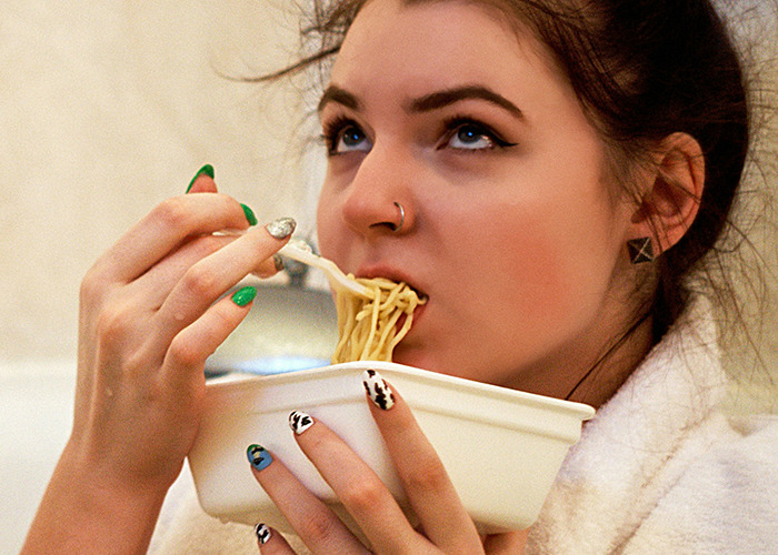 Young woman eating noodles from a container, showing the risks associated with processed foods as death machines warning. - 35