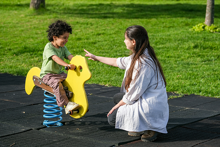 Child playing on a yellow spring rider with local babysitter in park, showcasing family trust and care outdoors.